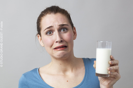 Junge Frau mit einem Glas Milch in der Hand verzieht das Gesicht: Wer unter einer Laktoseintoleranz leidet, reagiert auf den enthaltenen Milchzucker mit Blähungen und Bauchschmerzen.